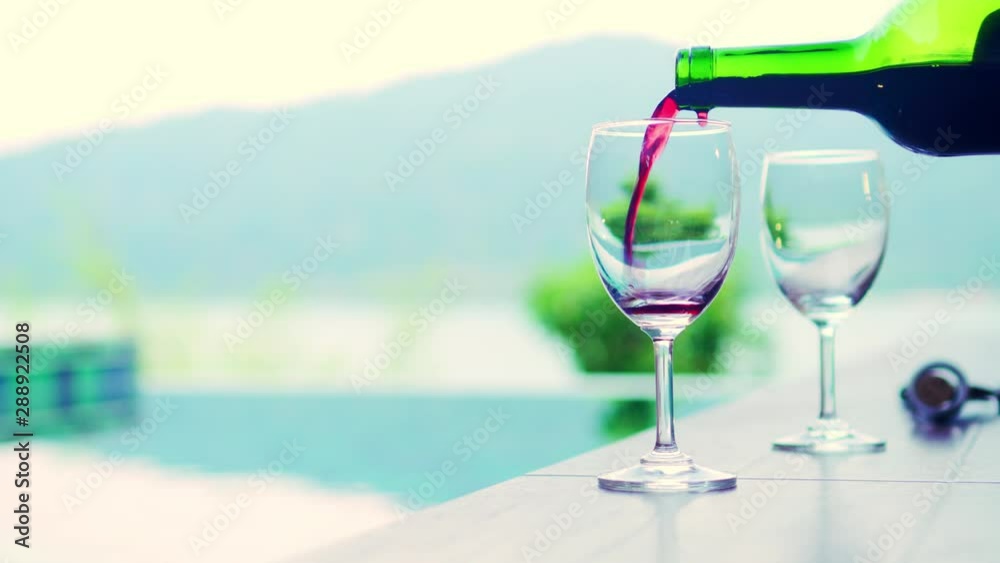 Pouring an excellent red wine in a glass near swimming pool at resort in weekend. Luxury lover romance tourism concept. Pouring an excellent red wine in a glass near swimming pool at resort in weekend. Luxury lover romance tourism concept.