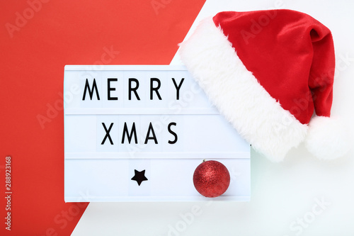 Lightbox with words Merry Xmas and red santa hat on colorful background