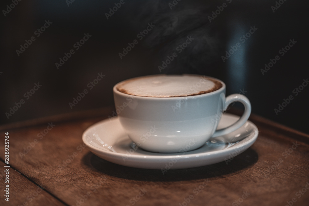 Hot coffee, cappuccino In a white cup with art foam. Near the window on the wooden table at the coffee shop Hot coffee, cappuccino In a white cup with art foam. Near the window on the wooden table at the coffee shop