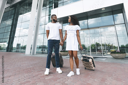 Glad african man and woman going out of airport building