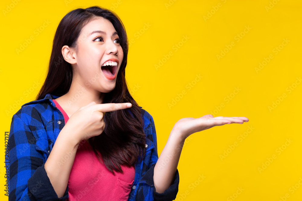 Fototapeta premium Charming beautiful young woman point finger and look at beautiful product. Beautiful lady get surprised, shocked when see product on palm. Pretty girl feel happy. advertising, commercial. copy space