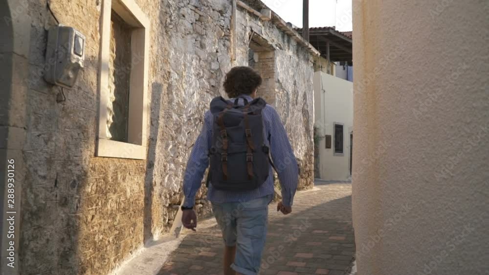 The camera follows a man with a backpack walking in the old city of Greece The camera follows a man with a backpack walking in the old city of Greece