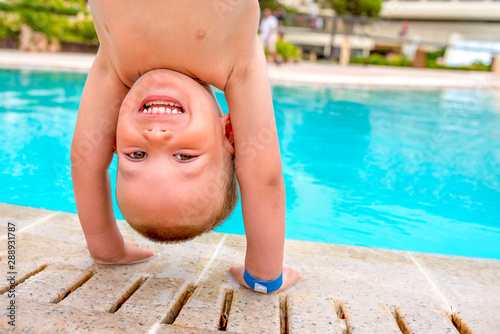 Adorable little boy standing upside down in front of swimming pool