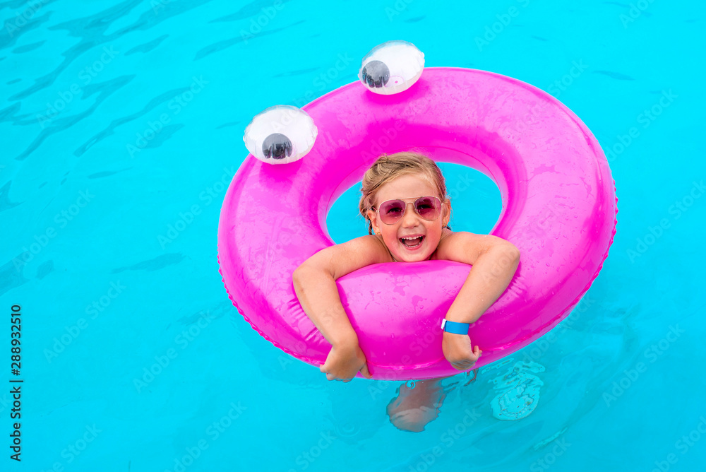 Adorable little girl playing with inflatable pink ring in swimming pool on summer vacation