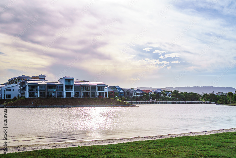 Wide panoramic view of Emerald Lakes residences across the lake, on a blue sky background during a beautiful sunset. Wide panoramic view of Emerald Lakes residences across the lake, on a blue sky background during a beautiful sunset.