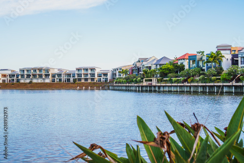  Wide panoramic view of Emerald Lakes residences across the lake, on a blue sky background during a beautiful sunset. Gold Coast, Australia.