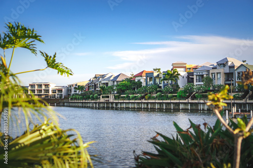  Wide panoramic view of Emerald Lakes residences across the lake, on a blue sky background during a beautiful sunset. Gold Coast, Australia.
