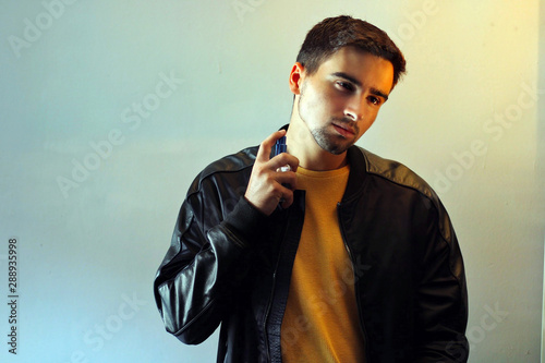 Young man using perfume or cologne on a gray background.