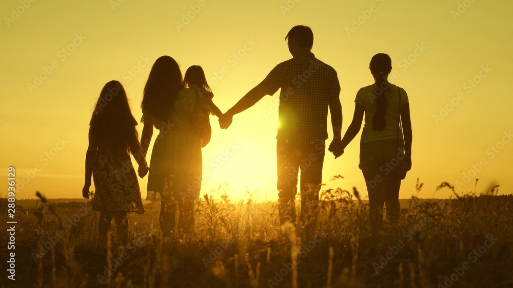 happy family walks in the field in sunset light. dad mom and daughters are walking in the park in light of sun. children and parents travel on vacation. happy father carries a child