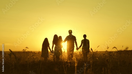 happy family walks in the field in sunset light. dad mom and daughters are walking in the park in light of sun. children and parents travel on vacation. happy father carries a child photo