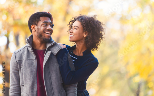 Portrait of happy afro couple cuddling over autumn background