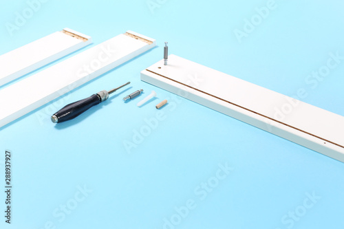 tools for assembly of flat packed furniture on blue background. white diy funiture parts with a screwdriver and screws top view. Relocation or moving into new house concept with copy space photo