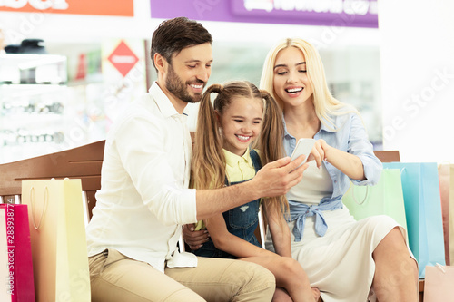 Family Using Smartphone Sitting In Mall Center After Shopping
