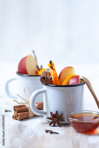 wo white metal mugs with ingredients for hot mulled wine - traditional christmas beverage. Ripe apple and orange, spices and honey. Corkscrew to open wine bottle. Holiday festive mood, rustic style