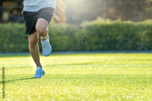 Runner athlete feet running on beautiful grass field.Male jogging workout with sunlight background.Wellness,Sport athlete active lifestyle concept.Copy space empty blank.