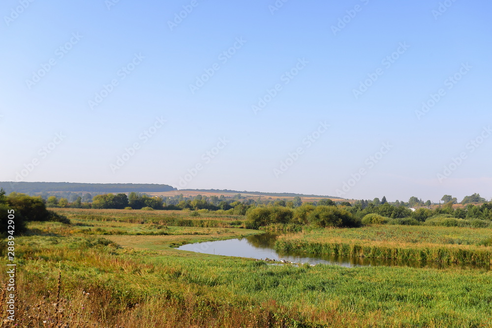 Summer rural landscape with small river, bright blue sky, white clouds reflect in the water. Have a nice summer day