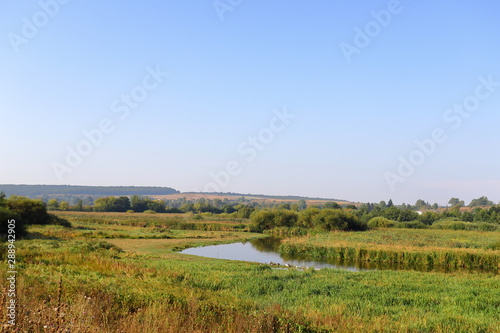 Summer rural landscape with small river  bright blue sky  white clouds reflect in the water. Have a nice summer day