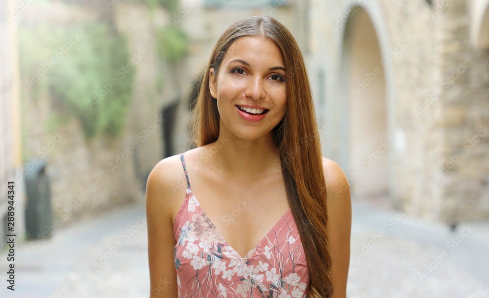 Smiling fashion dressed woman walking in the streets of a small medieval town in Italy.
