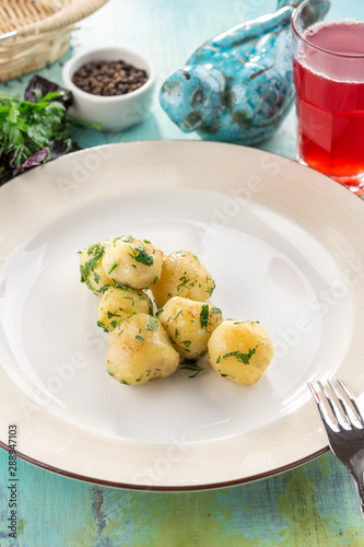 young boiled potatoes with dill in oil on white plate on blue wooden table