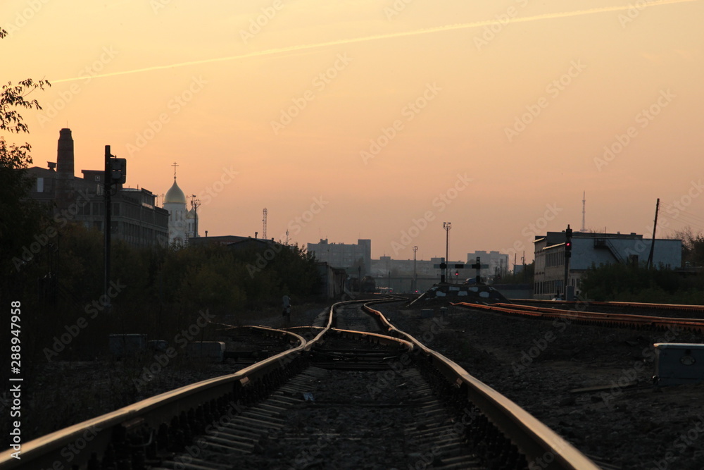 railway arrow  in sunset light with background of city and pink sky