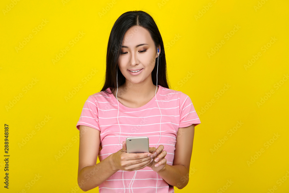 Beautiful young woman with smartphone and earphones on yellow background