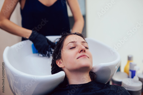 Hairdresser washing hair of a beautiful young woman in hair salon.