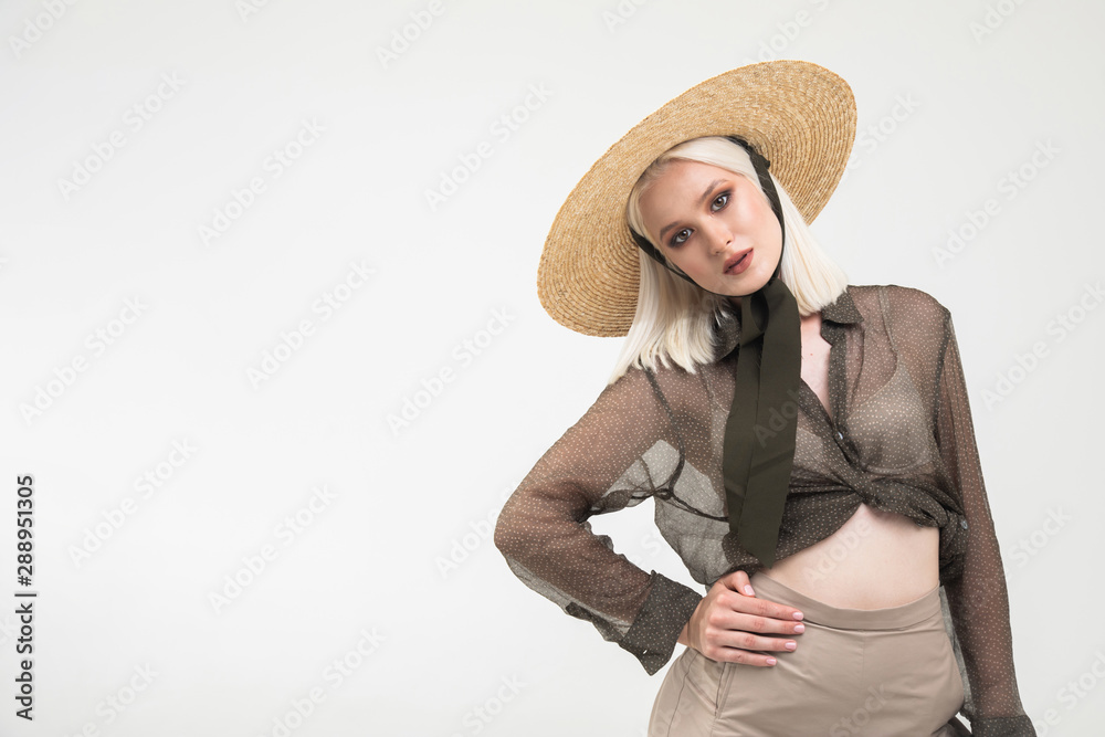 Pretty blonde in transparent blouse and straw hat posing with her hand on waist isolated white background copyspace Pretty blonde in transparent blouse and straw hat posing with her hand on waist isolated white background copyspace