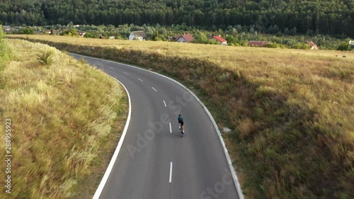 Aerial drone view of man cycling in downhill along country road.