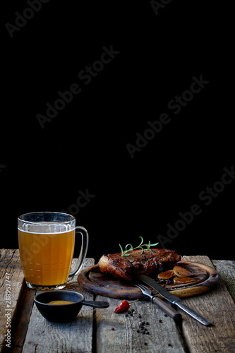 Still life with a big fried steak, a glass of beer, mustard and cutlery on an old wooden tabletop, the concept of Oktoberfest and St. Patrick's Day