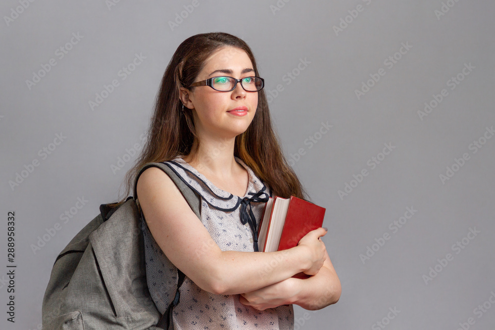 Education. A young woman or teenager wearing glasses, with a backpack on her back, holding a book in her hands and looking away. Copy space Education. A young woman or teenager wearing glasses, with a backpack on her back, holding a book in her hands and looking away. Copy space