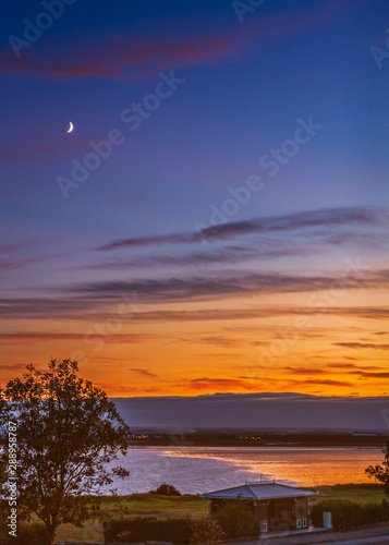 A new moon above Sandwich Bay as the golden sunset reflects into the low tide of the bay.