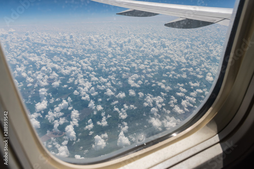 View from the plane's porthole on the plane's wing, the ground below and the clouds of a summer day in flight