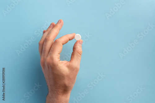Male hand holding one pill. Flat lay.