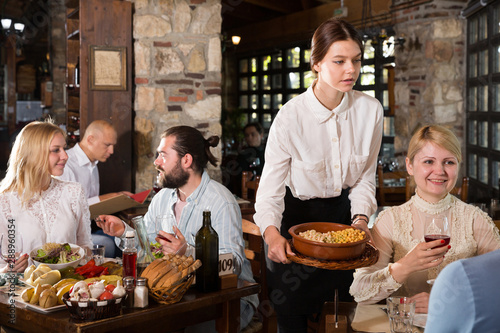 Young female waiter serving country restaurant guests