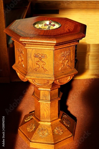 Sunbeams streaming in on old traditional eight sided wooden baptismal font with Fototapet