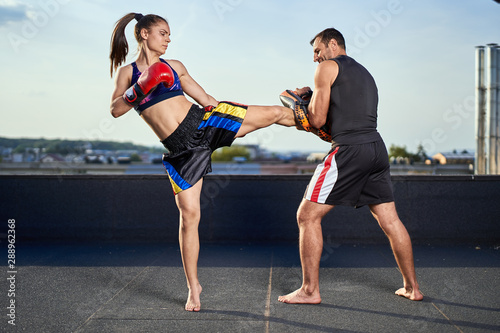 Young woman kickboxer in urban environment, training