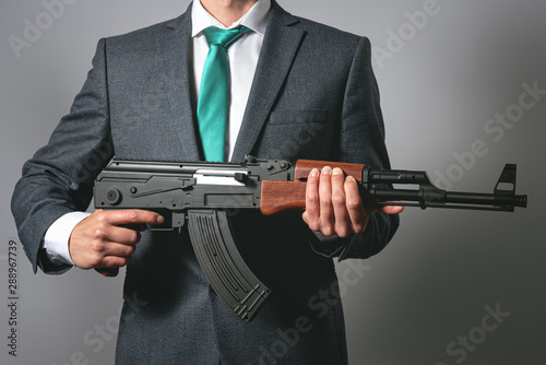 Businessman with a assault rifle airgun on a gray background. Business protection. Threat to business concept. © Dmitriy