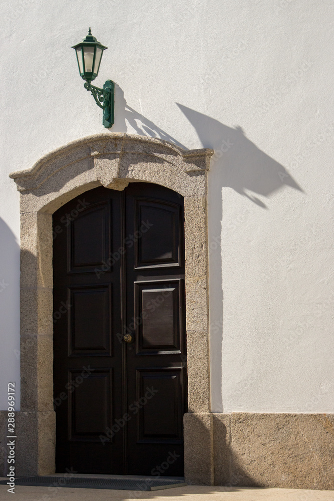 Closed entrance to church with green lantern above door. Street lamp on  white wall of old building with wooden door. Ancient exterior design in  Europe. Doorway with lamp. Vintage architecture details. Stock
