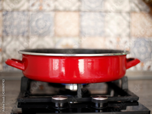 Red frying pan on the gas stove. Cooking in a red saucepan on the fire. Photo on kitchen