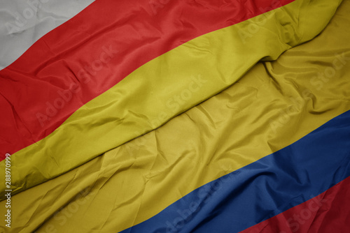 waving colorful flag of colombia and national flag of south ossetia.