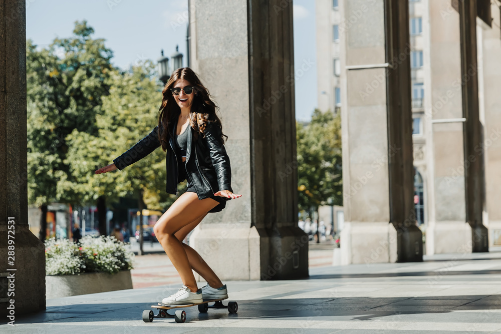 Beautiful young skater woman riding on her longboard in the city. Stylish girl in street clothes rides on a longboard.