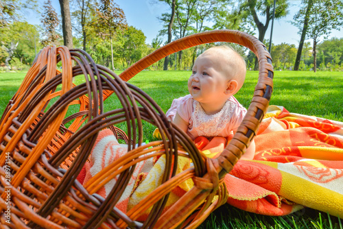 Little child in a park on green grass on a litter in a straw basket.