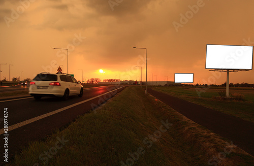 Samochód osbowy na drodze, zachód słońca, bilbord reklamowy, tekst.