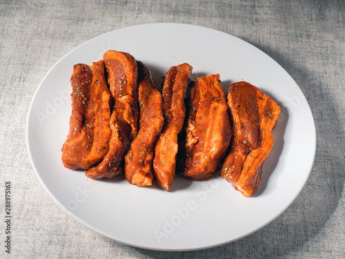Fresh uncooked pork belly slices in Korean style marinate on a white plate.