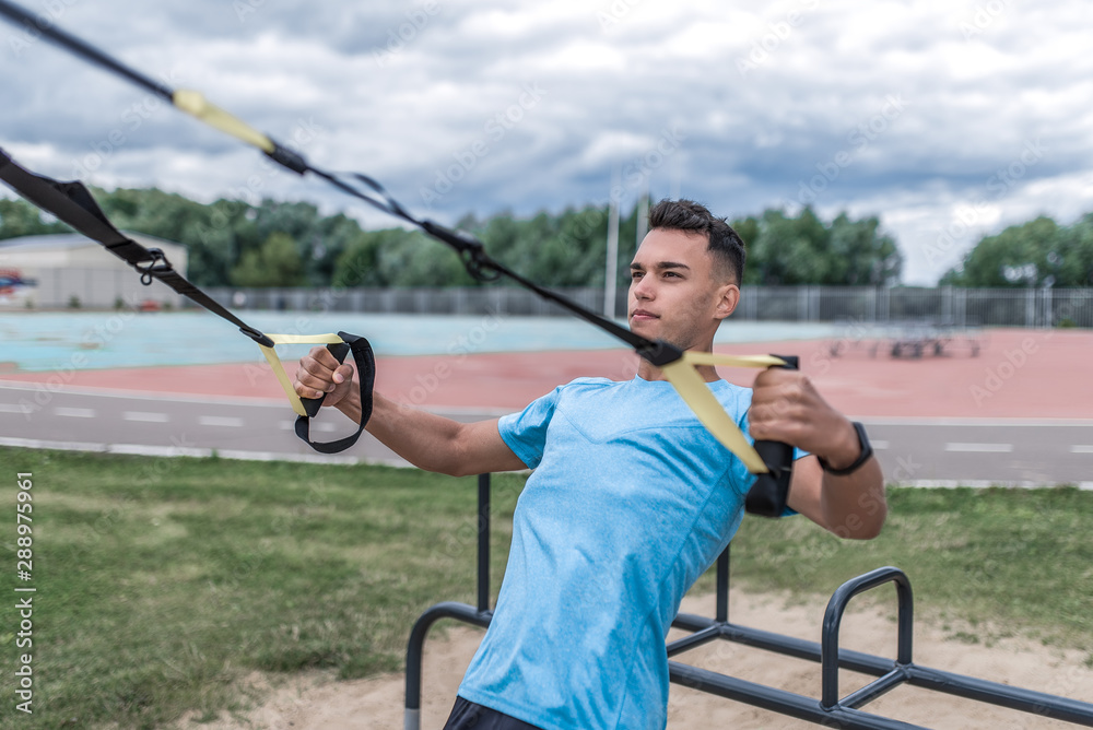 Athletic man athlete training on loops, active straps traction, summer city training, motivation for doing fitness sports workout. Active lifestyle young people, powerful stylish man trainer teacher. Athletic man athlete training on loops, active straps traction, summer city training, motivation for doing fitness sports workout. Active lifestyle young people, powerful stylish man trainer teacher.