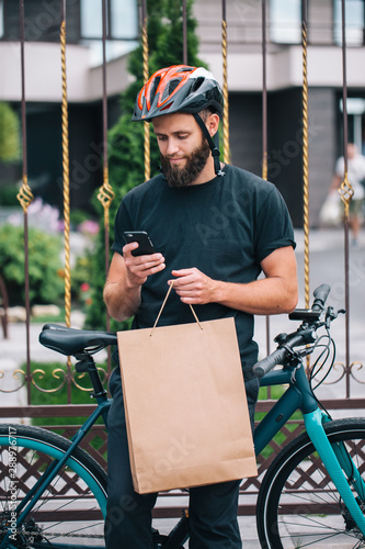 Bearded male courier with bicycle delivery food service at home. Shopping paper bag with copy space for your text or advertising content. No name shopping bag