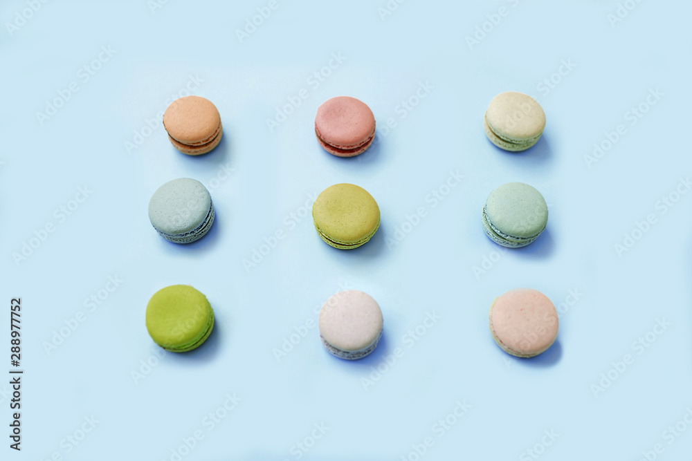 Top view of sweet macaroon biscuits lying in three lines on light blue background. Top view of sweet macaroon biscuits lying in three lines on light blue background.