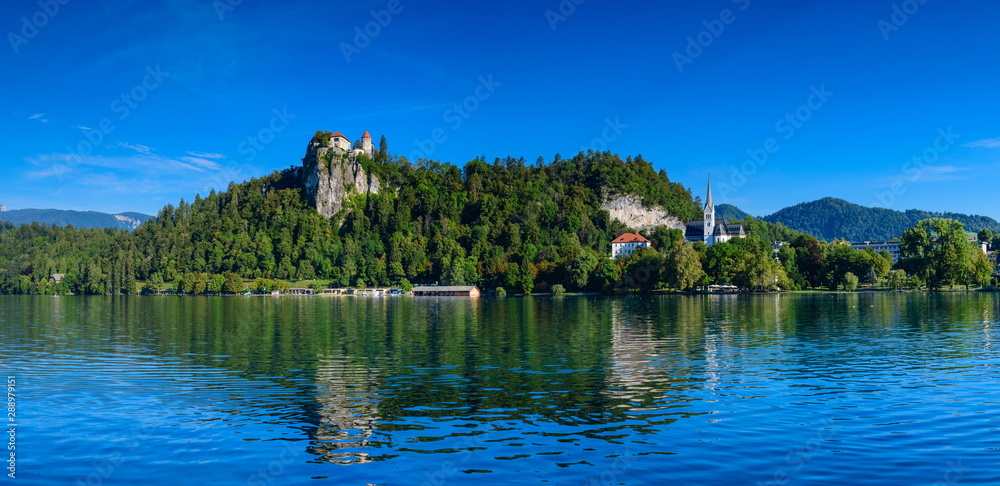 Beautiful panoramic view of the shore of Lake Bled with a medieval castle and the Catholic Church of St. Martin.