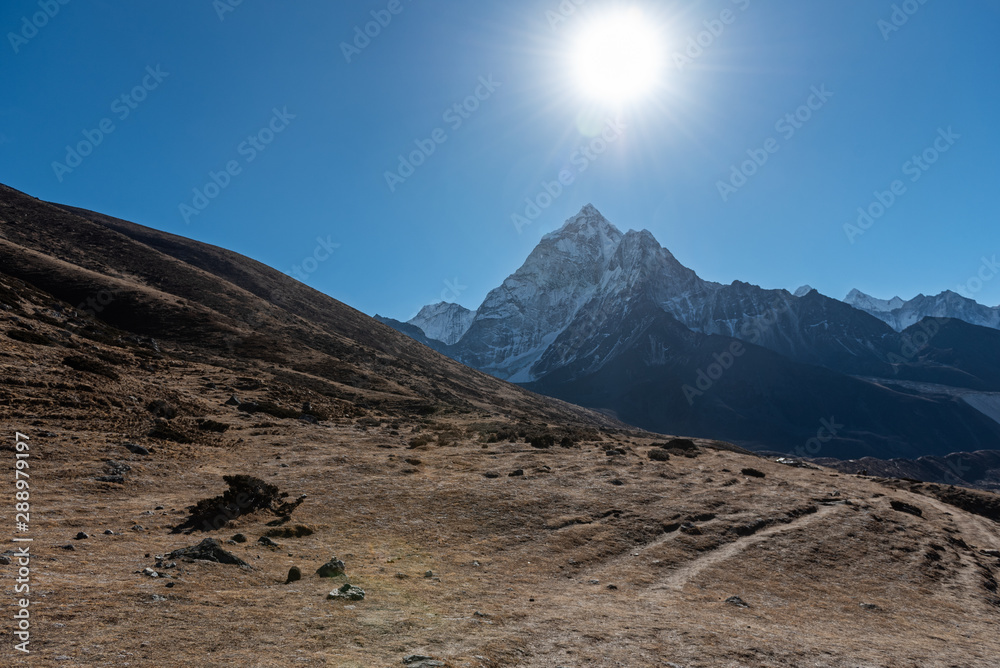 The dry winter brings out brown colours that cover the hilly landscape with tall sharp mountains in the background on a clear sunny day in the Nepalese Himalayas