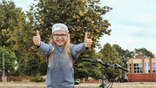 An 11 year old girl shows her thumbs up in a good mood next to her bicycle in the summer. photo